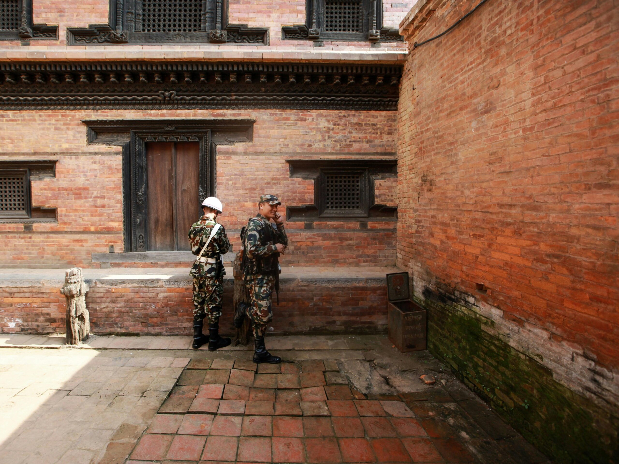 Two soldiers in uniforms standing near a historic brick building, featuring traditional architecture.